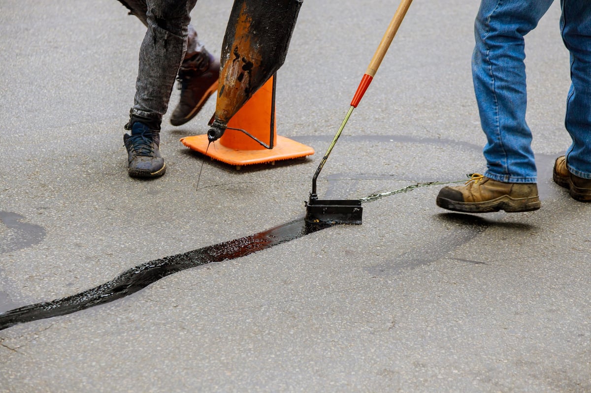 Road surface restoration work in the worker performs on road patcher work on the repair of cracks by filling and sealing with coated by bitumen emulsion asphalt surface