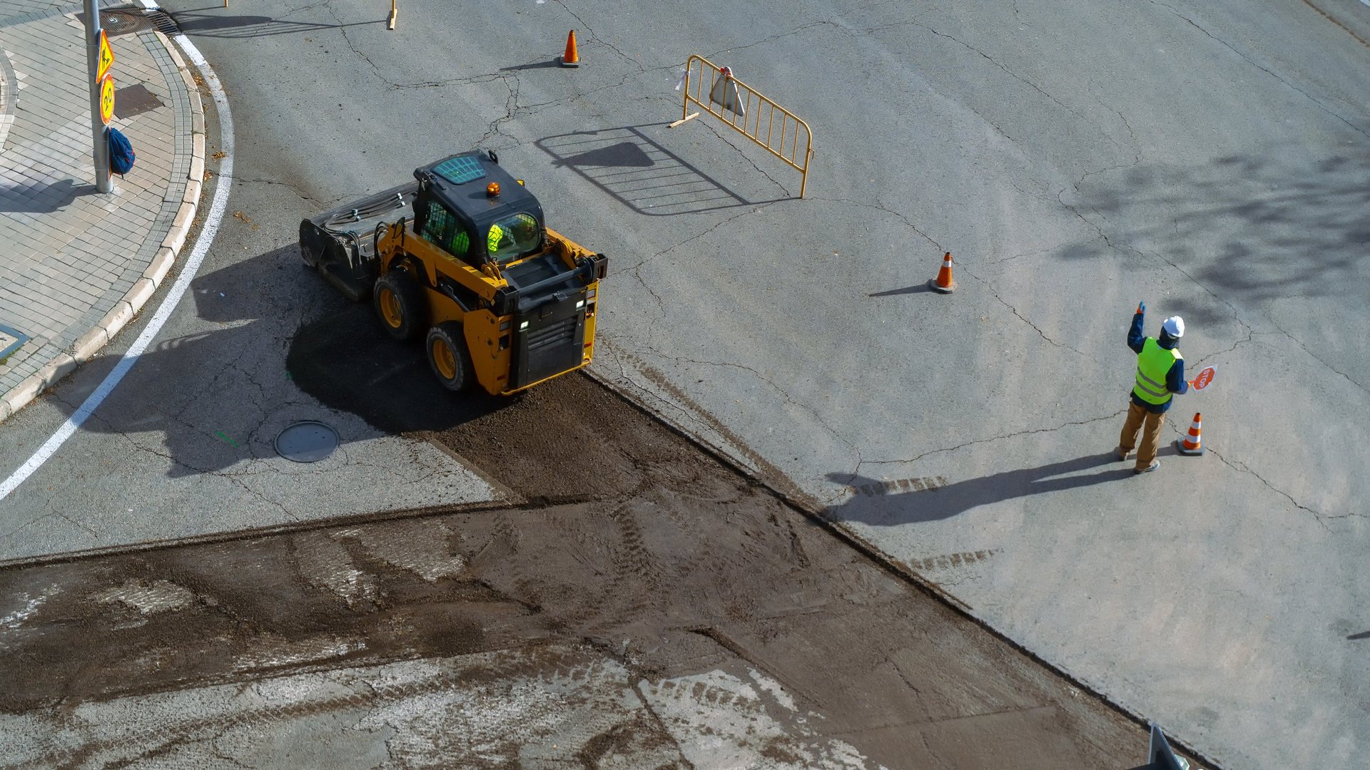 Construction worker guiding a skid steer loader paving a road section in Lakeway, TX