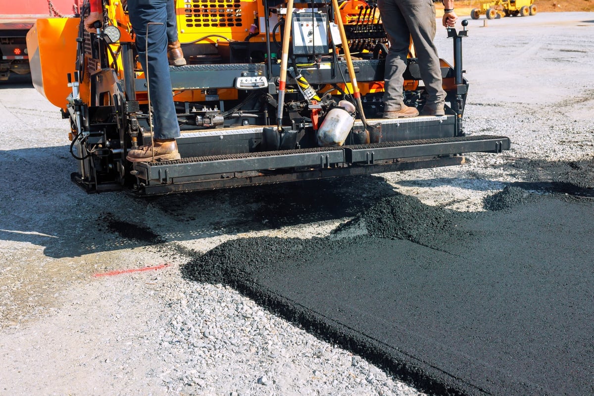 Workers operate paving machine to lay new asphalt on residential neighborhood roadway — professional asphalt paving in Austin, Leander, and Central Texas by Austin Premier Paving