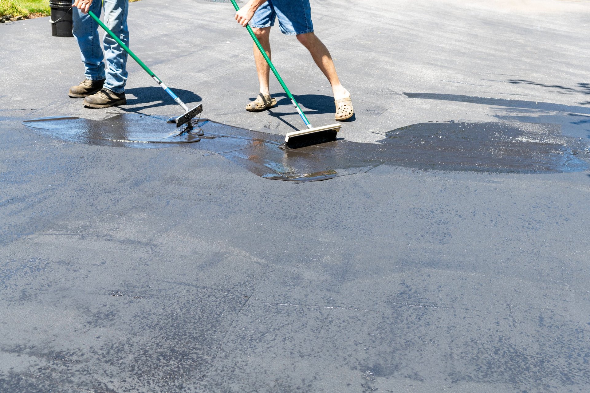 two men sealing asphalt driveway with brush and squeegee only legs showing