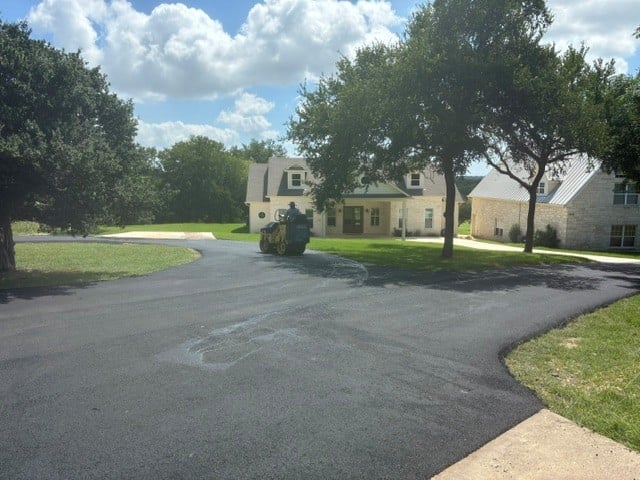Curved driveway leading to a two-story beige house with mature trees on a sunny day